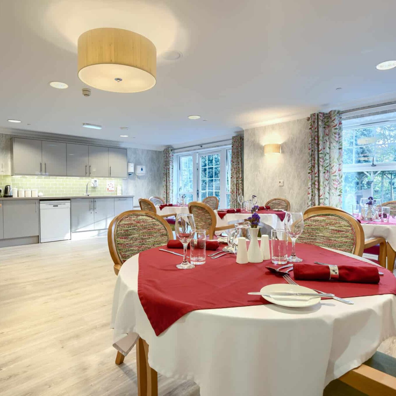 Dining room with tableware and kitchen area at Woodland Grove Care Home in Loughton