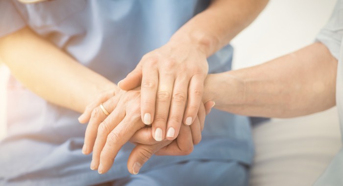 Close-up of young carer and elderly resident holding hands